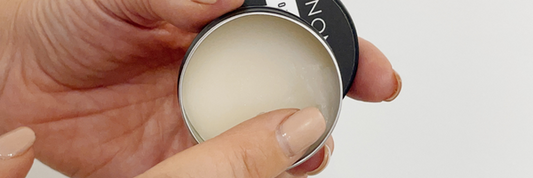 Finger applying solid body scent perfume balm from a black tin