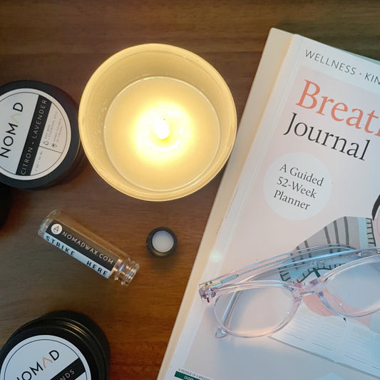 Lit Nomad candles, matches, eyeglasses and yoga journal on wood nightstand