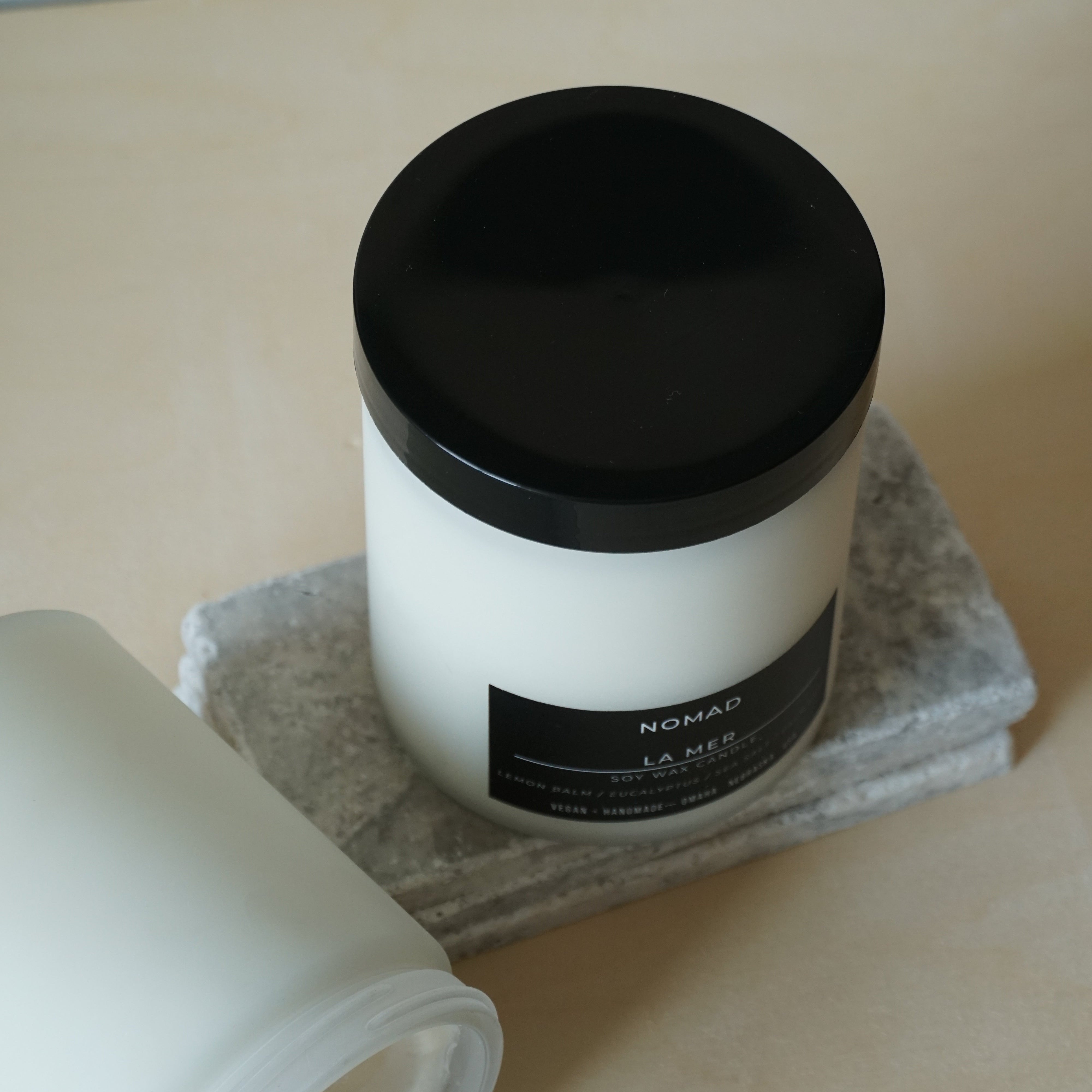 White container candle with black lid on a beige surface