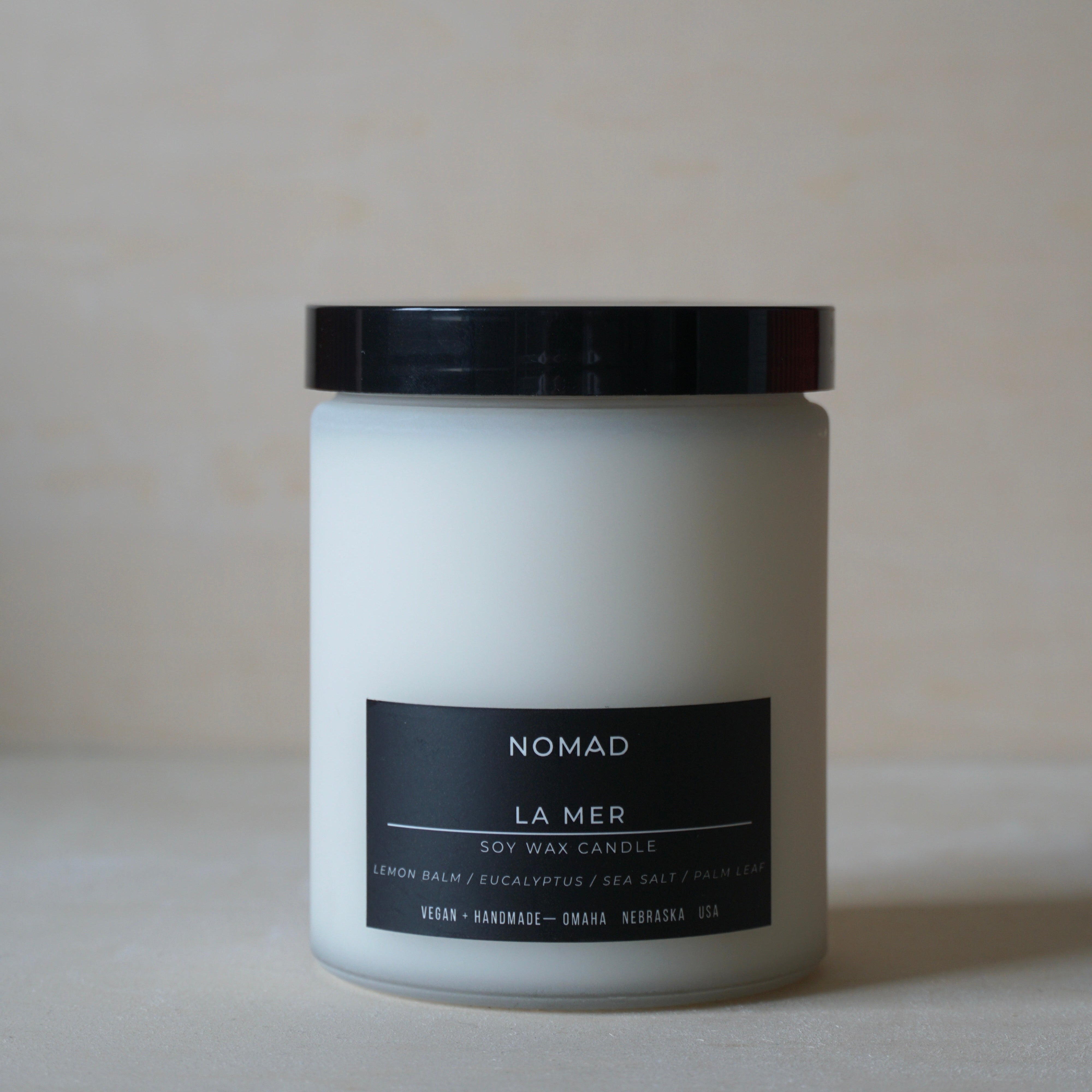 White candle soy candle with black lid and label on a neutral background