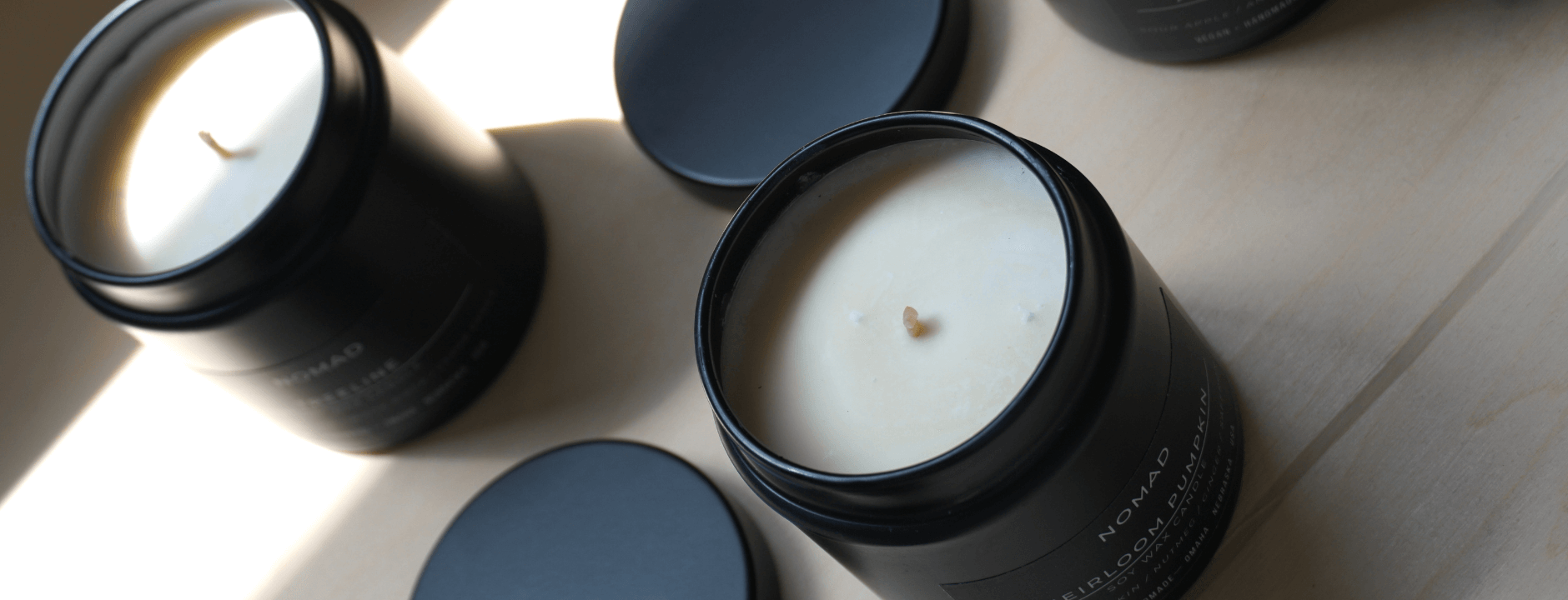 Two black candles with lids on a light wooden surface