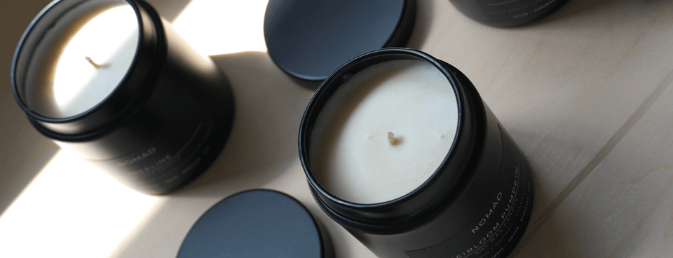 Two black candles with lids on a light wooden surface